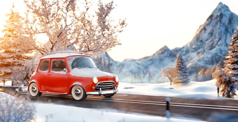 red car on snowy road with mountains behind it